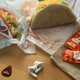 Taco Bell tacos on table with hot sauce packets, guitar pick, and AirPod headphones
